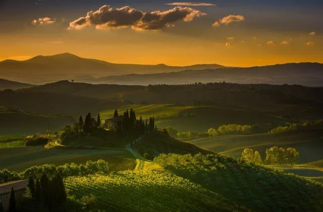 A Tuscan villa on a hilltop at sunset, surrounded by rolling fields and dark cypress trees