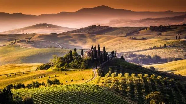 A Tuscan farmhouse on a hill at dusk, surrounded by misty fields and rows of crops