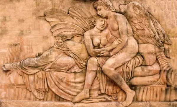 A classical frieze of two winged lovers embracing on draped cushions, in warm terracotta stone