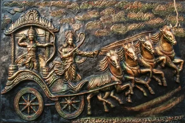 Krishna guides Arjuna's chariot as a team of horses charges forward, in dark bronze relief