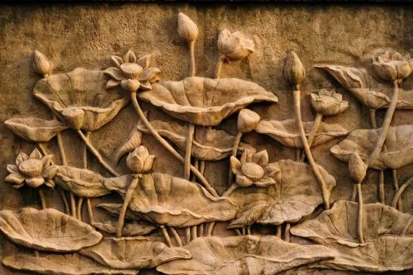 Lotus blooms, buds and broad leaves rise from a pond in a deep sandstone-carved relief