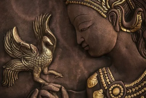 A serene crowned profile gazes at a golden bird held in her hands, carved against deep chocolate brown