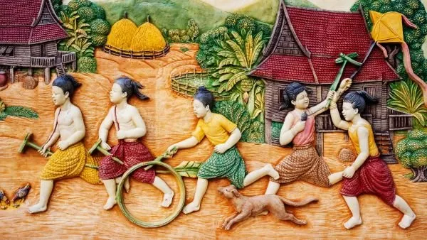 Village children race with hoops and sticks past stilt houses and haystacks, in bright painted relief