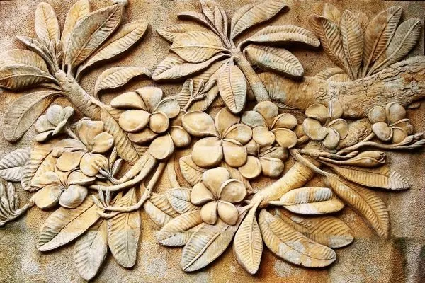 Clusters of frangipani blossoms and long leaves spread across a pale sandstone relief