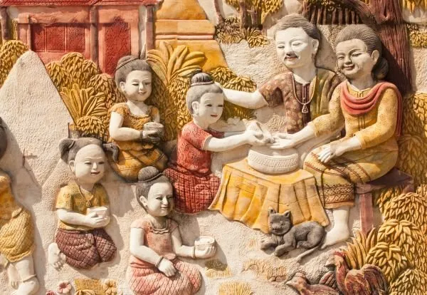 Grandparents and children gather around a shared meal with a cat at their feet, in softly painted relief