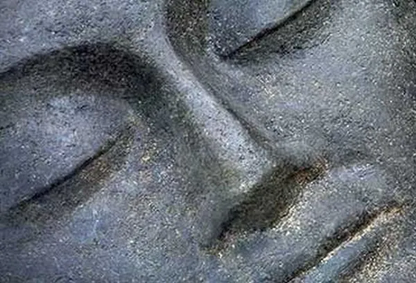 An extreme close-up of a serene stone face with closed eyes, in textured slate grey