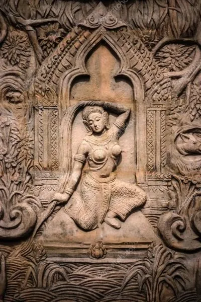 A celestial dancer seated within a carved temple arch, surrounded by scrolling foliage in warm brown stone
