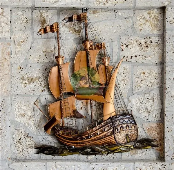 A three-masted sailing galleon in copper and wood tones, set against a pale stone-block wall