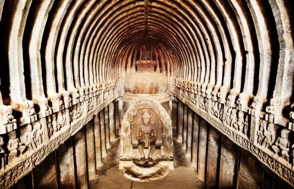 A rock-cut prayer hall with a ribbed vaulted ceiling and pillared aisles leading to a seated figure