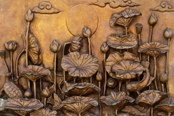 Lotus leaves and buds rise beneath a full moon and curling clouds in burnished bronze relief
