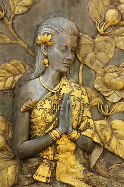 A serene woman with hands joined in prayer, framed by large gilded leaves and blooms