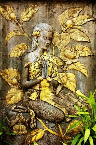 A kneeling woman in prayer, her gilded robe and the surrounding leaves catching the light