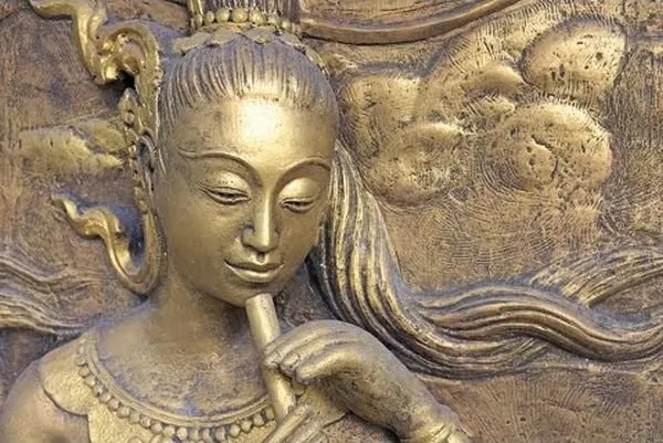 A close-up of a crowned maiden playing a flute, in gleaming antique-gold relief