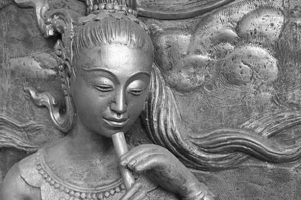 A close-up of a crowned maiden playing a flute, in cool silver-grey relief