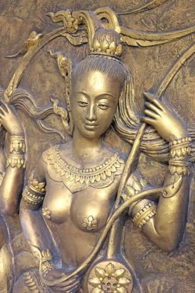 A crowned celestial maiden holding a bow and lotus wheel, in burnished gold relief