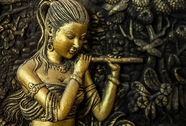 A golden maiden plays a flute against a dark carved garden, in rich black and gold relief