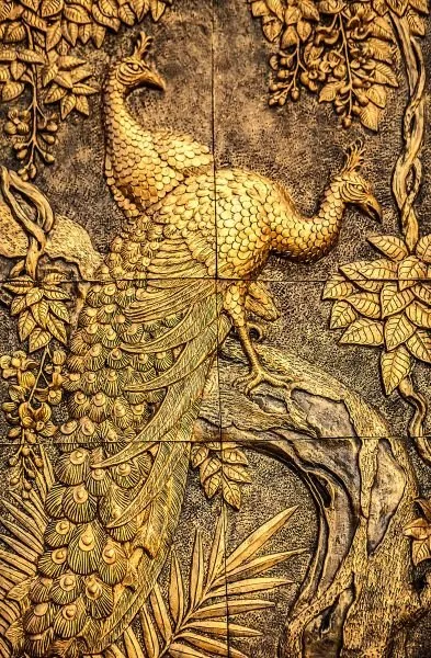A gilded peacock perches on a curving branch, its long tail sweeping down among carved leaves