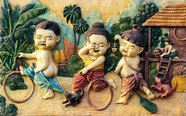 Three cheerful village children play with hoops and a dog outside a thatched hut, in bright painted relief