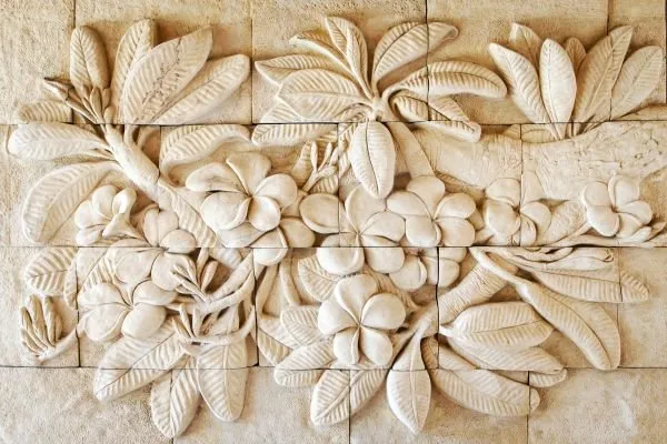 Frangipani blossoms and broad leaves spread across a tiled sandstone-look relief panel