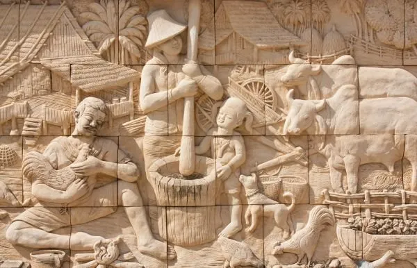 Villagers pound grain, tend buffalo and feed chickens in a tiled sandstone relief