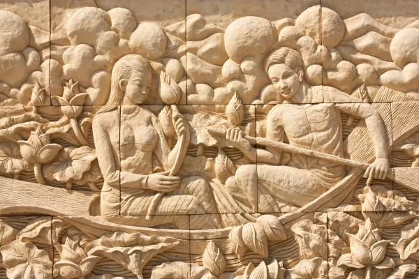A woman and a boatman glide through lotus flowers in a long boat, in warm sandstone relief