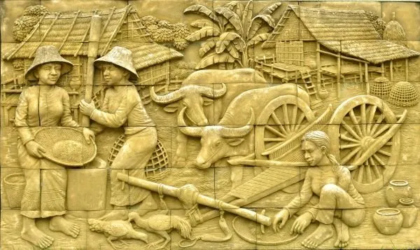 Farmers winnow grain, buffalo pull a cart and villagers work the harvest in golden-yellow relief