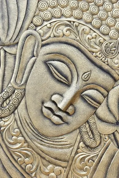 A serene Buddha face with closed eyes beneath a crown of carved curls and swirling ornament
