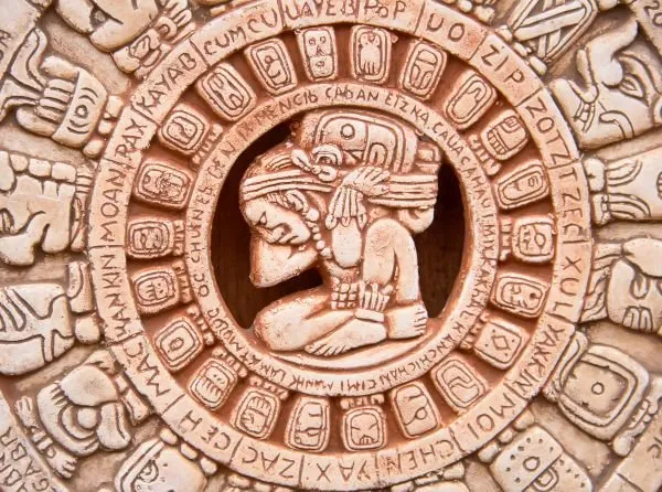 A seated figure at the centre of a circular Mayan-style glyph calendar, in terracotta relief