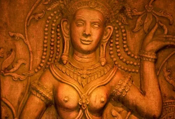 A crowned temple goddess with beaded hair and jewellery, glowing in deep amber stone
