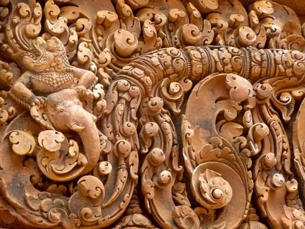 Deeply carved temple scrollwork with a small figure among the curls, in rich terracotta red