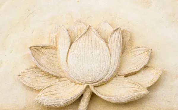 A single open lotus flower carved in soft cream stone, with wide space around it