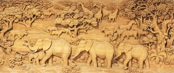 Elephants walk in procession while deer and other animals roam the trees, in a wide golden-wood relief