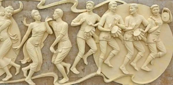 A line of dancers and drummers celebrate together in a flowing cream relief