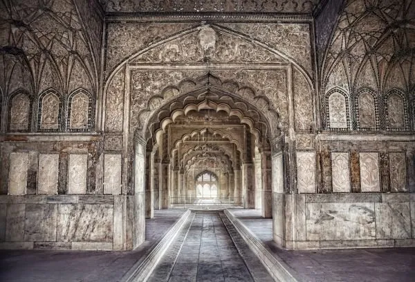A long Mughal-style corridor of carved arches recedes into soft light, creating deep perspective