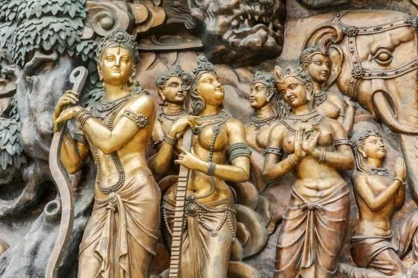 A crowned prince leads a group of jewelled women past an elephant, in gilded relief