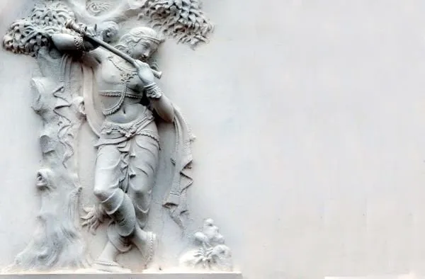 Krishna plays his flute beneath a leafy tree, carved in pure white on a wide, plain ground