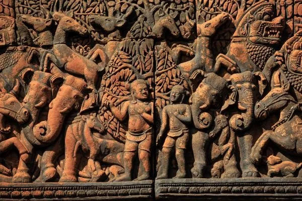 Elephants, horses and riders march in crowded rows across a weathered terracotta relief