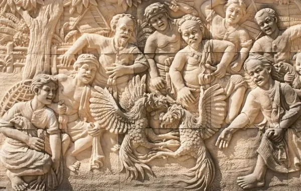 Villagers crowd around two roosters, cheering and gesturing, in a pale sandstone relief