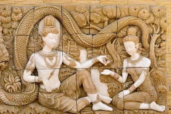 A crowned couple sit in conversation beneath a coiling serpent, in a warm tiled sandstone relief