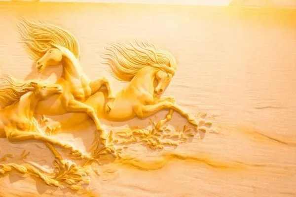 Golden horses with windswept manes race across soft, sunlit sand in a warm amber relief