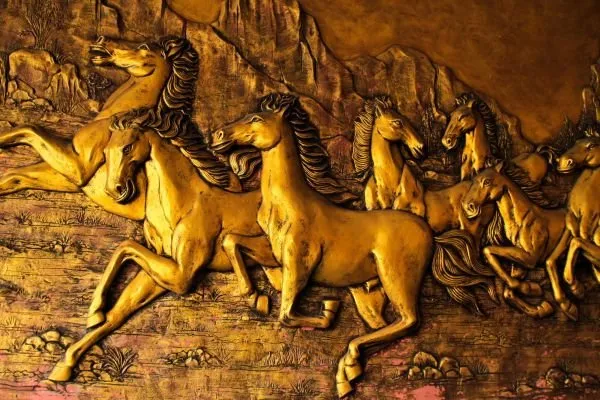 A herd of golden horses charges forward with flying manes, in a dramatic gilded relief