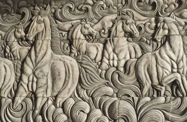 Muscular horses rise from swirling waves in a grey stone relief