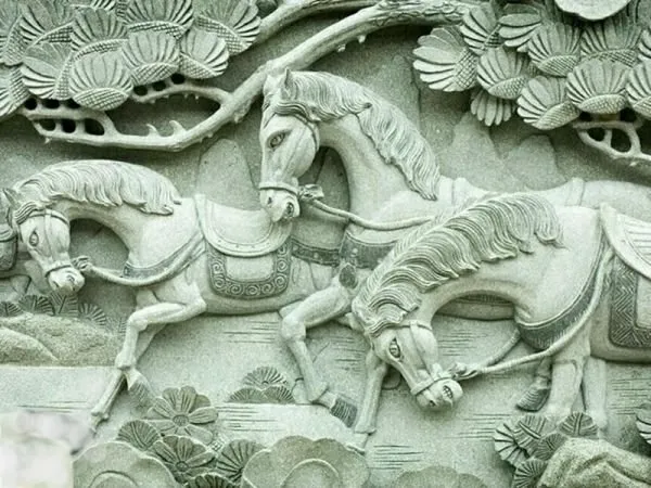 Saddled horses gallop beneath pine branches in a cool jade-green stone relief
