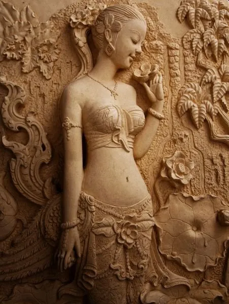 A graceful maiden raises a flower to her face amid carved lotus leaves, in warm sandstone