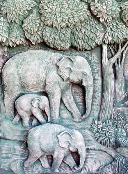 An elephant mother walks with two calves beneath a leafy tree, in cool teal-grey relief