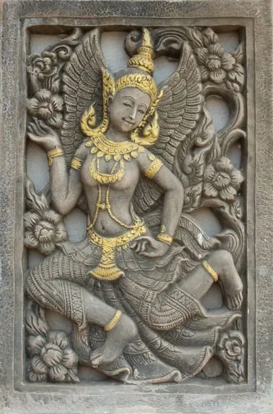 A winged celestial dancer with gilded crown and jewellery, within a carved grey stone frame