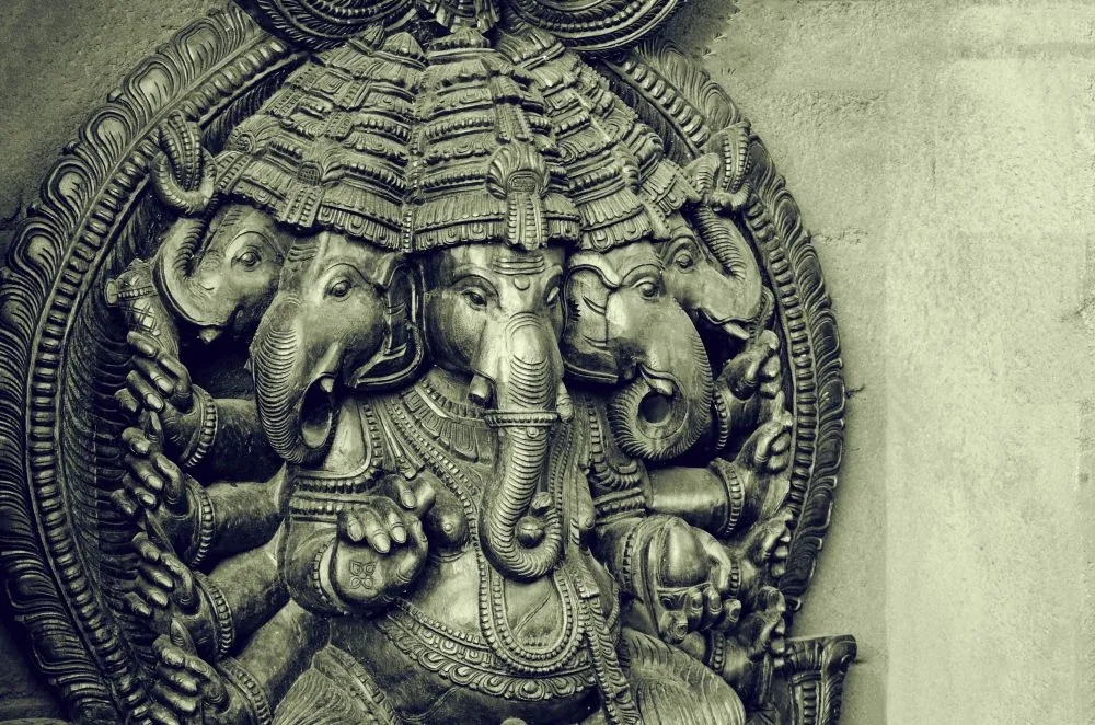 A monochrome photograph of a carved, multi-headed Ganesha sculpture with intricate temple detailing
