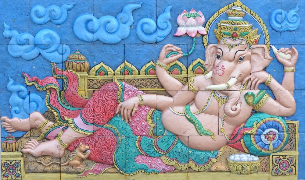 A colourful relief-style Ganesha reclining among stylised blue clouds, with lotus and ornate details