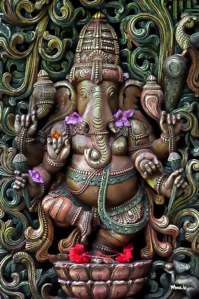 A photograph of a carved temple Ganesha surrounded by green-bronze scrollwork, with red flowers at his feet