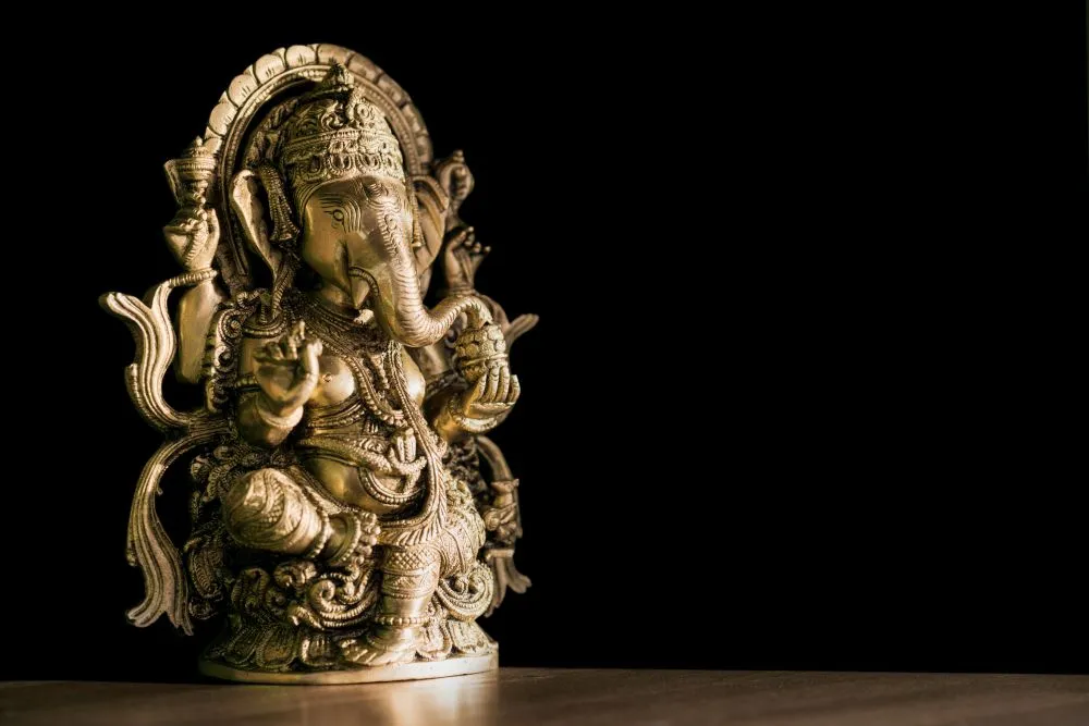 A photograph of a brass Ganesha statue lit by a single spotlight against deep black